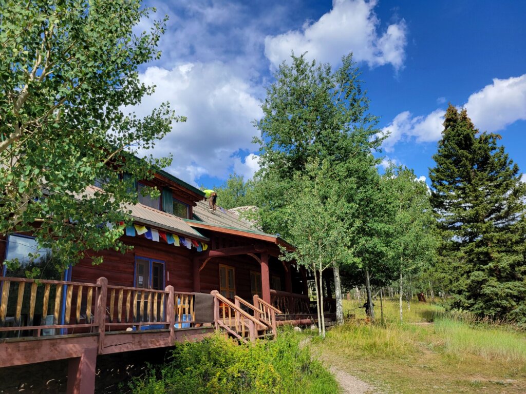 A photograph of a retreat center building at Vallectios Mountain Retreat Center with prayer flags on a day with clouds and blue sky.