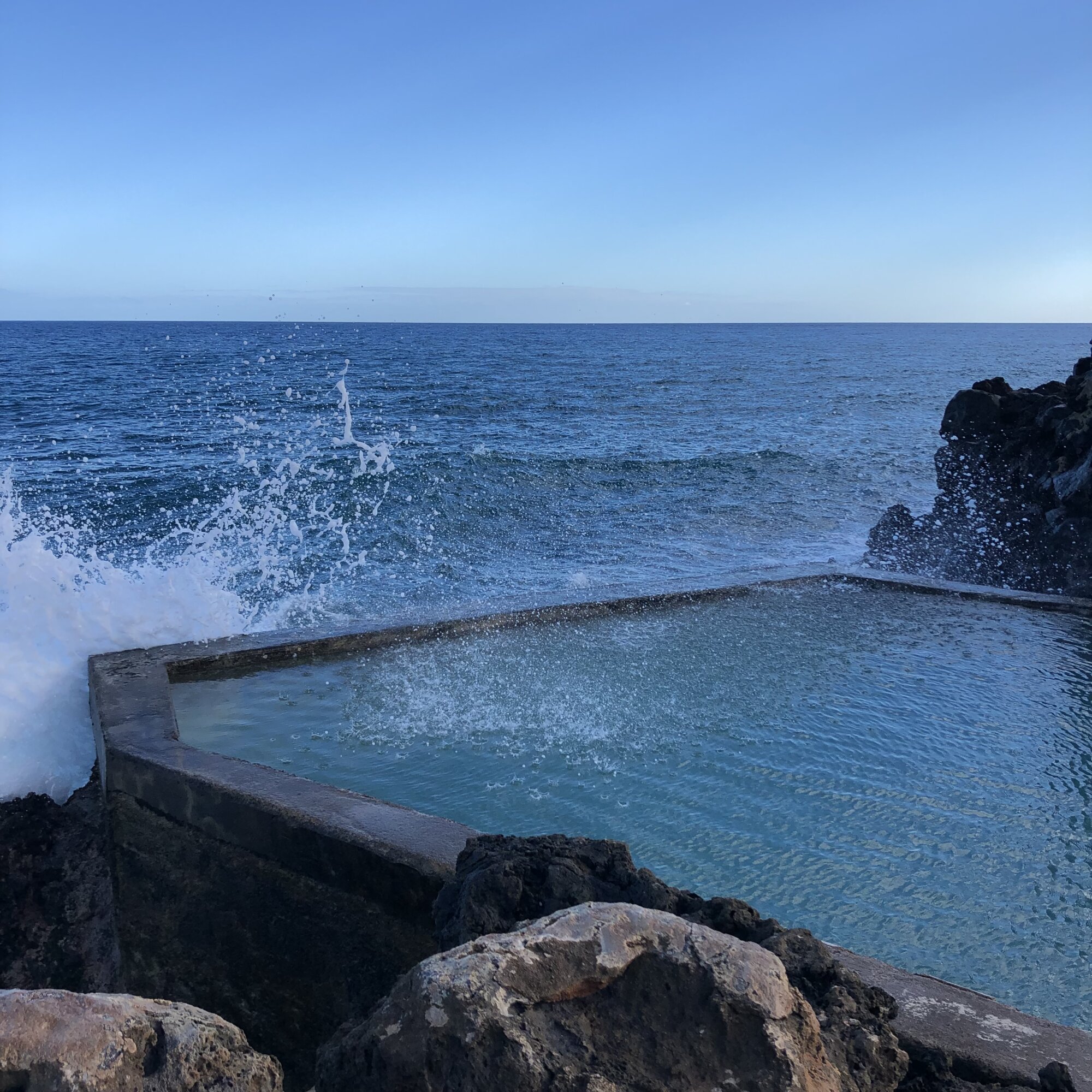 A small pool on the edge of the ocean, with a wave mixing ocean water with the water in the pool.