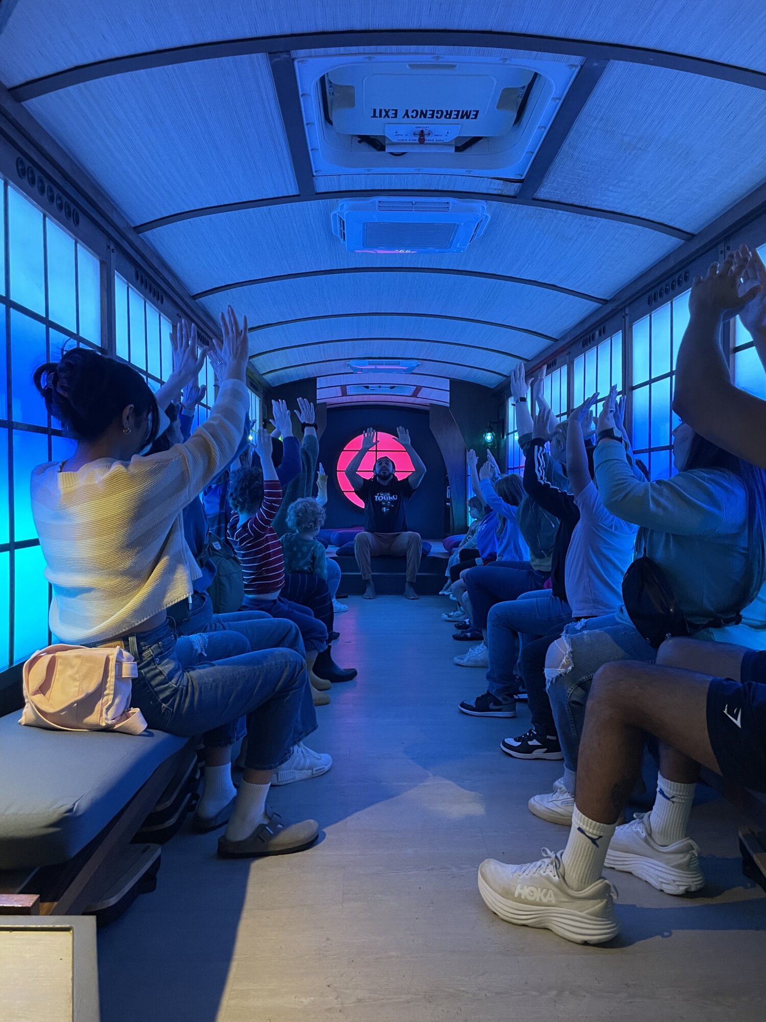 Children led by a teacher doing a physical activity on a colorfully illuminated and decorated school bus.