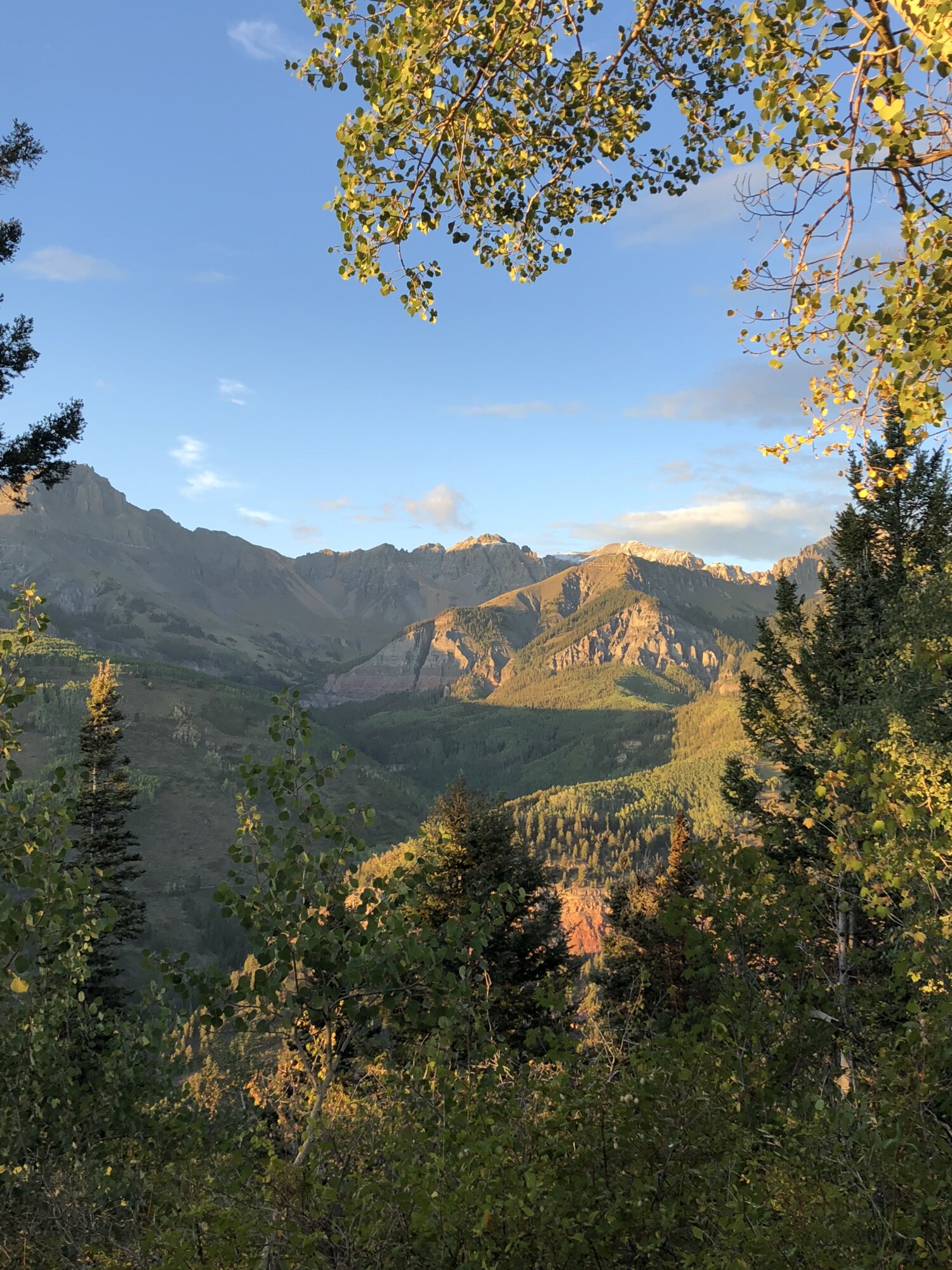 A panorama of forested mountains at the golden hour, with light illuminating some areas against other shadowed areas.