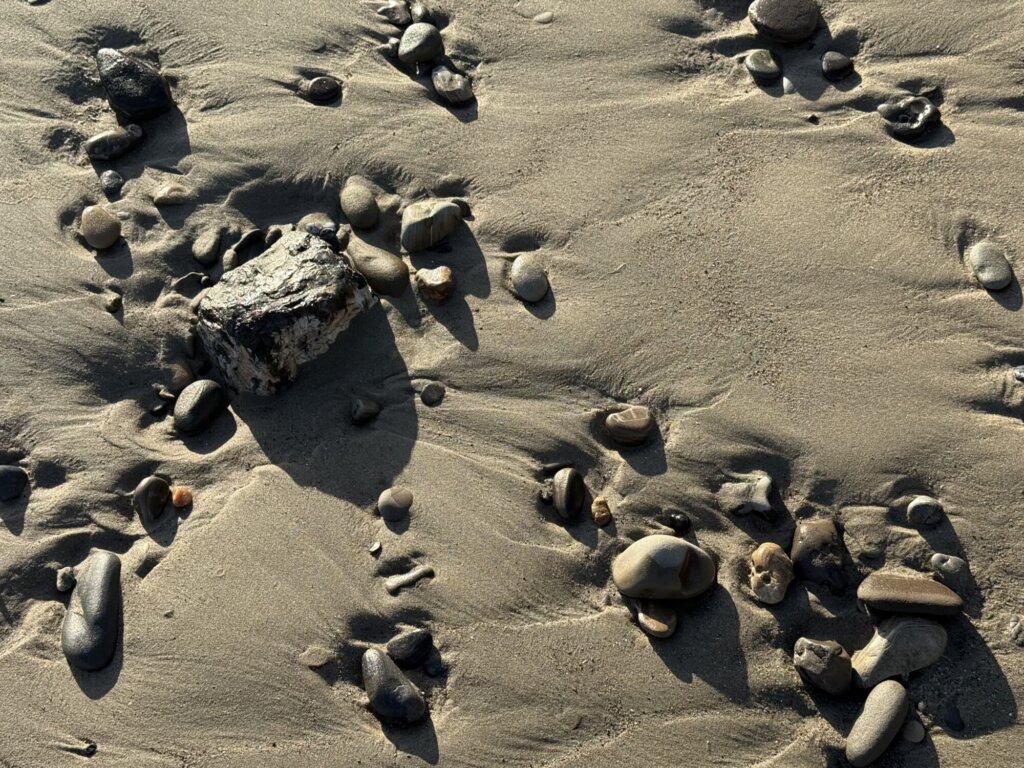 A beach with pebbles, with the sand showing traces of past waves.